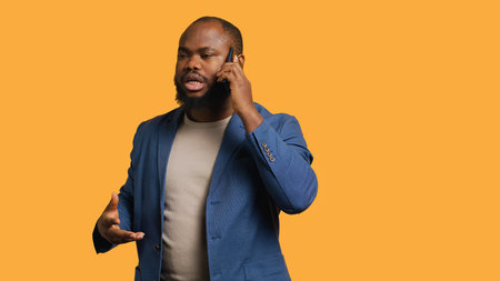 Irked african american man fighting with friends during telephone call, isolated over studio background. Outraged person arguing with mates during conversation on mobile phone, camera Aの写真素材