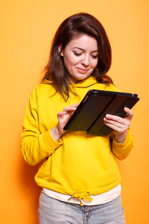 Close-up of caucasian woman utilizing tablet with a touch screen. Smiling female individual holding digital device and looking at screen, working on online related projects.の写真素材