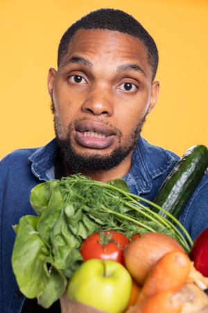 Young person feels pleased with his paper bag full of fresh groceries, preparing to cook a vegan recipe. African american model confident with his zero waste way of living, healthy eating.の写真素材
