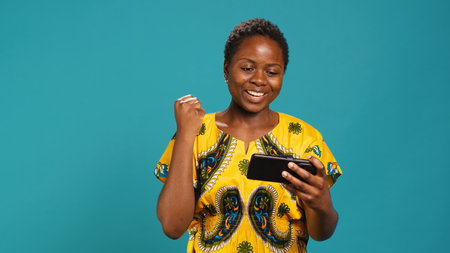 Happy pleased girl winning an online videogames competition, having fun playing e sport tournament against blue background. Woman plays internet gaming, celebrates her victory. Camera A.の写真素材