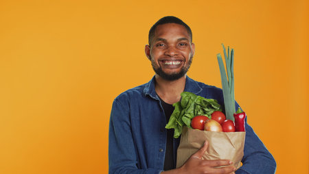 Portrait of vegan person carrying a paper bag filled with fresh groceries, supporting local farming and homegrown produce. Male model enjoying shopping spree at bio supermarket. Camera A.の写真素材