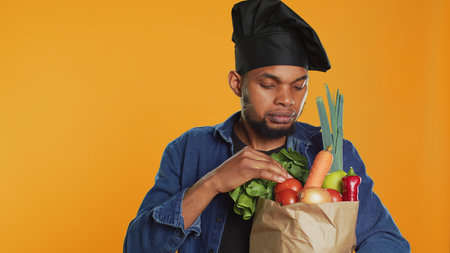 Pleased vegan chef cooking a meal with eco friendly local produce, shopping for organic groceries to prepare a special recipe. Happy cook advertising ethically sourced food. Zero waste. Camera A.の写真素材