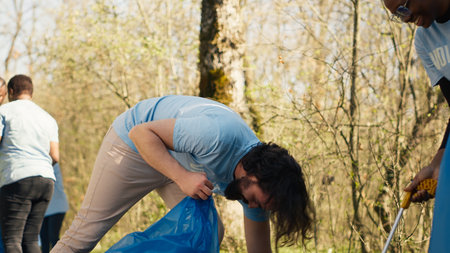 Team of volunteers collecting rubbish to fix pollution problem within the habitat, protect the natural environment. Activists doing voluntary work to clean the woods from trash. Camera B.の写真素材