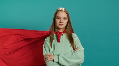 Happy young girl portraying superhero flying with cape fluttering in wind, isolated over studio background. Portrait of upbeat heroic woman posing as hero in costume, camera Aの写真素材