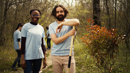 Portrait of two activists clearing up the forest surroundings by collecting garbage, growing new trees and picking up trash. Eco friendly enthusiasts preserving environments and wildlife. Camera B.の写真素材