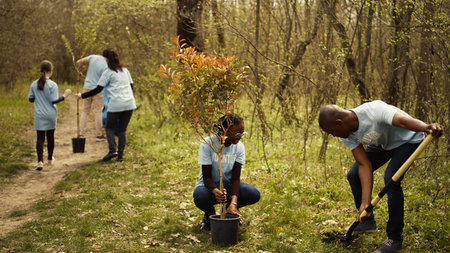 Team of activists planting trees to conserve natural ecosystem and forest environment, digging holes after collecting rubbish. Volunteers taking action and preserving the woods habitat. Camera B.の写真素材