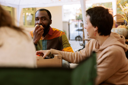 Young black man biting a fresh organic apple at outdoor food tasting festival. Multicultural couple sampling and enjoying various locally grown fruits and vegetables at farmers market.の写真素材