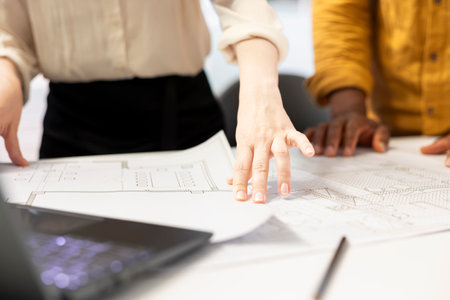 Professional clients and their real estate agent engage in an office planning session, reviewing blueprints and discussing investment opportunity for urban workspace leasing. Close up.の写真素材