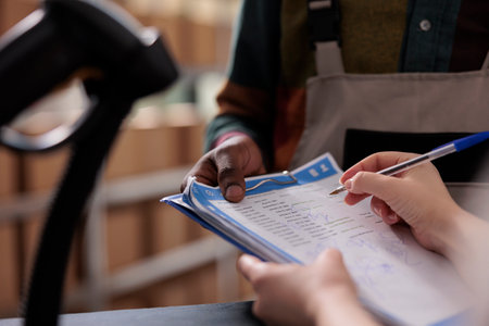 Warehouse manager signing cargo checklist, discussing merchandise inventory working at goods quality control. Diverse team preparing customers orders for delivery in storehouse. Close upの写真素材