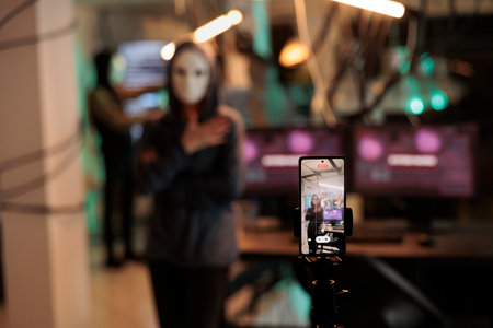 Hacking thief filming live ransomware video late at night, threatening to expose important information after breaking encryption. Spy with anonymous mask hacking database system with trojan virus.の写真素材