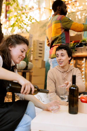 Local merchant pouring fresh organic wine for female shopper at street food festival. Caucasian woman vendor offering natural homemade products to customer at farmers market.の写真素材
