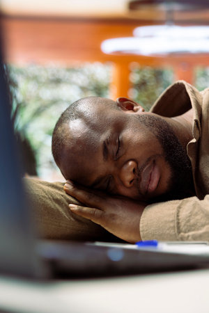 Tired entrepreneur takes a nap on laptop at his home office setup, falling asleep while he works on business management. Man working under pressure and feeling overworked.の写真素材