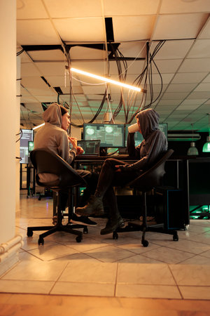 Young hackers coding trojan virus program to hack system, IT specialists programming illegal firewall encryption. Two cybercriminals developing malicious software late at night.の写真素材