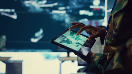 Army soldier reviews targets on a satellite world map to ensure global protection, works on tablet in military command center. Private examines battlefield data for intelligence. Close up. Camera B.の写真素材
