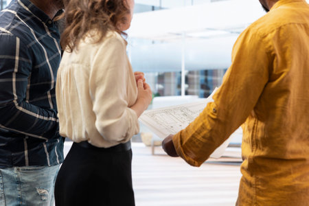 Real estate agent guiding clients on an office hunt with layout blueprints, modern architectural plans and discussing potential property investment. Relocation in a high class urban setting.の写真素材