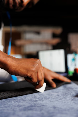 Extreme close up of couturier meticulously checking business suit pants seam in professional atelier studio. Experienced suitmaker finishing comissioned stylish custom made sartorial outfitの写真素材