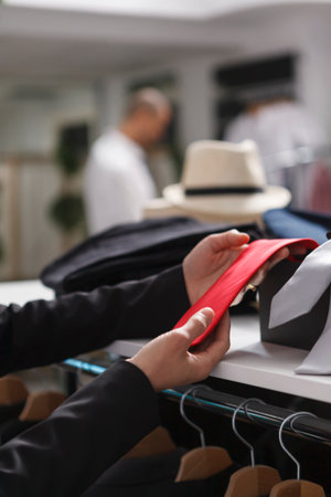 Woman seller hands putting red tie on accessory shelf while organizing merchandise in clothing store closeup. Mall employee arms examining garment while working in apparel outletの写真素材