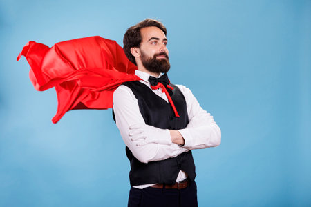 Young man in suit and red cape posing on camera, acting confident as a superhero from cartoon. Powerful determined person wearing red mantle, prepared to save and rescue people.の写真素材