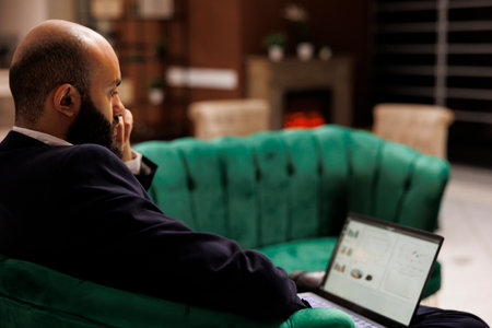 Businessman review notes on laptop, sitting in lounge area at hotel and preparing for upcoming corporate meeting. Working on conference speech, excellent amenities and services.の写真素材