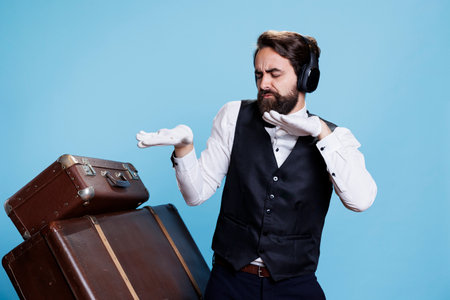 Silly hotel porter listens to music on camera, having fun with songs and dance moves. Skilled elegant doorkeeper feeling funky and using headphones, works in hospitality industry.の写真素材