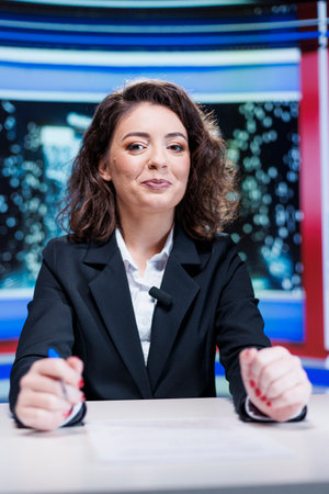 Show presenter hosting media segment to discuss about live daily events, talking about celebrities and global issues. Television host creating news report using headlines, broadcasting on tv.の写真素材