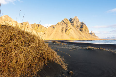 Rocky mountain hills meeting the ocean, fantastic icelandic landscapes with black sand beach. Nordic stokksnes peninsula with vestrahorn mountain range and beachfront, sightseeing.の写真素材
