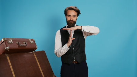 Hotel concierge does timeout symbol in studio, asking for a break working in hotel and tourism industry. Elegant doorkeeper in formal attire indicating pause gesture with hands, professional job.の写真素材