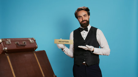 Hotel staff shows reception pointer on camera, leading guests in the right direction or area. Professional luxury doorman working in tourism travelling sector, showing front desk indicator.の写真素材