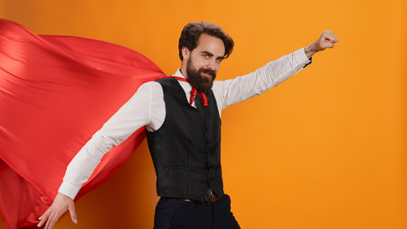 Confident waiter with red hero cape posing as a superhero on camera, determined to serve clients. Superhuman restaurant employee serving food and drinks, hero character costume with mantle.の写真素材