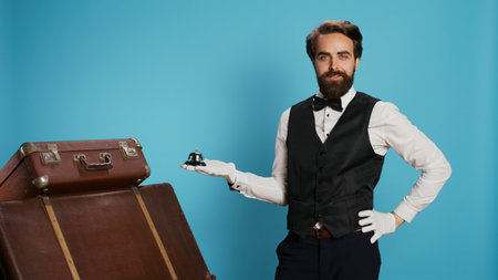 Hotel concierge shows service bell ringing for assistance, showcasing tourism and hospitality industry concept. Male porter helping with suitcase pile, luxury experienced doorman.の写真素材