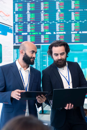 Diverse group of business specialists solve their daily tasks in control room with big screen,...