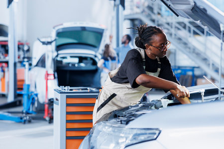 African american woman in car service using professional mechanical tool to repair broken radiator. Experienced mechanic in garage fixing client automobile, ensuring optimal automotive performanceの写真素材