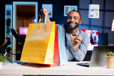 African american man filming fashion vlog, unboxing bags with internet order, showing subscribers purchases he recently got. Influencer presenting viewers new shopping acquisitionsの写真素材