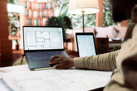 Businessman using digital tools to draft and plan office spaces to relocate, reviewing blueprints...