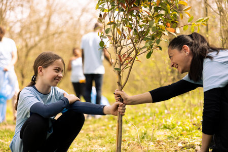 Mother and little girl working together on planting new trees, increasing vegetation and helping with reforestation. Happy people activists contributing to conservation project.の写真素材