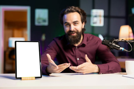 Tech specialist presenting mockup tablet to interested viewers, filming with professional mic. Man reviewing isolated screen digital device, recording with specialized equipmentの写真素材