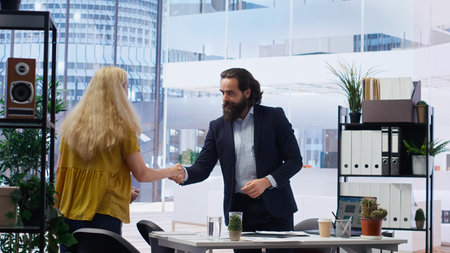 Portrait of cheerful financial advisor in office meeting with parent and child to provide personalized spending planning. Jolly agent in workspace doing handshake with customers, camera Bの写真素材
