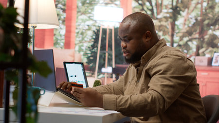 Business owner makes a payment with his card for online shopping at his home, electronic banking to buy resources for his startup. Entrepreneur purchasing something on laptop. Camera A.の写真素材