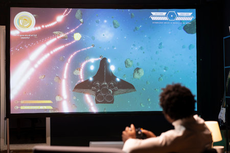 Man playing galaxy flying videogame on large smart TV, relaxing. Competitive gamer having fun on gaming console in stylish apartment living room, piloting spacecraft using gamepadの写真素材