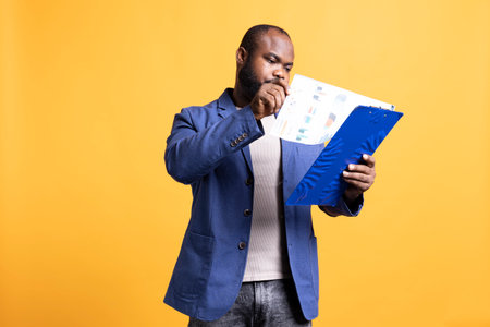 Man browsing though audit report pages, isolated over studio background. Employee reading clipboard with files containing economic graphs and figures, solving company tasksの写真素材