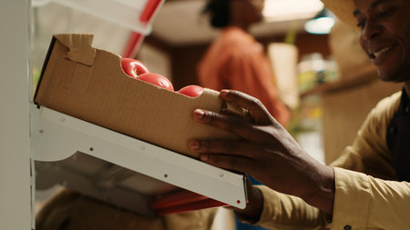 Local farmer placing crates with homegrown produce on shelves, working on fruits and vegetables restock for customers. Merchant carrying boxes of organic freshly harvested goods. Camera 1.の写真素材