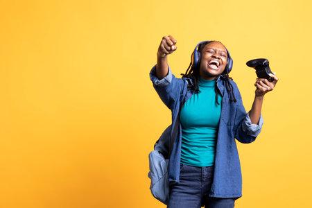 Euphoric african american teenager playing intense gaming console game, celebrating win, studio background. Ecstatic BIPOC young girl using controller, excited after being victorious in videogameの写真素材