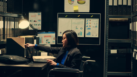 Law agent reviewing classified documents in archive room, searching for important clues from forensic evidence. Wheelchair user categorizing archived materials to facilitate investigation. Camera A.の写真素材