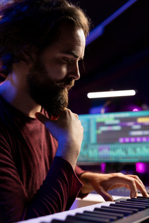 Artist thinking of new piano notes combinations to play on his electronic keyboard, recording music with daw software in home studio. Musician searching for inspiration in playing synthesizer.の写真素材