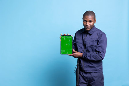 Male skilled agent presents an isolated mockup screen on tablet, showing chromakey layout against blue background. Security guard wearing uniform and baton in front of the camera.の写真素材