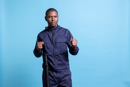 Professional security guard posing with clenched fists in studio, ready to throw punches while on duty. Male agent protecting the premises, taking safety measures and fighting if necessary.の写真素材