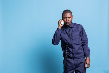 African american security guard patrolling the premises at night, using his flashlight to inspect the perimeter in the dark. Male agent examining the area with a lantern for safety.の写真素材