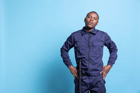 Security officer on patrol showing his authority in front of the camera, standing with hands on his hips against blue background. Serious confident agent in studio, proud of his work duty.の写真素材