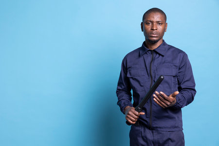 Skilled confident security officer holding a protection baton in his hands, preparing for any emergency defense or fight to safeguard the perimeter. African american guard on protecting duty.の写真素材