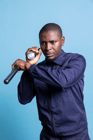 Trained security officer inspecting the premises with a flashlight and his baton, patrolling at night in the dark for safety control. Guard looking around with his lantern, public protection.の写真素材